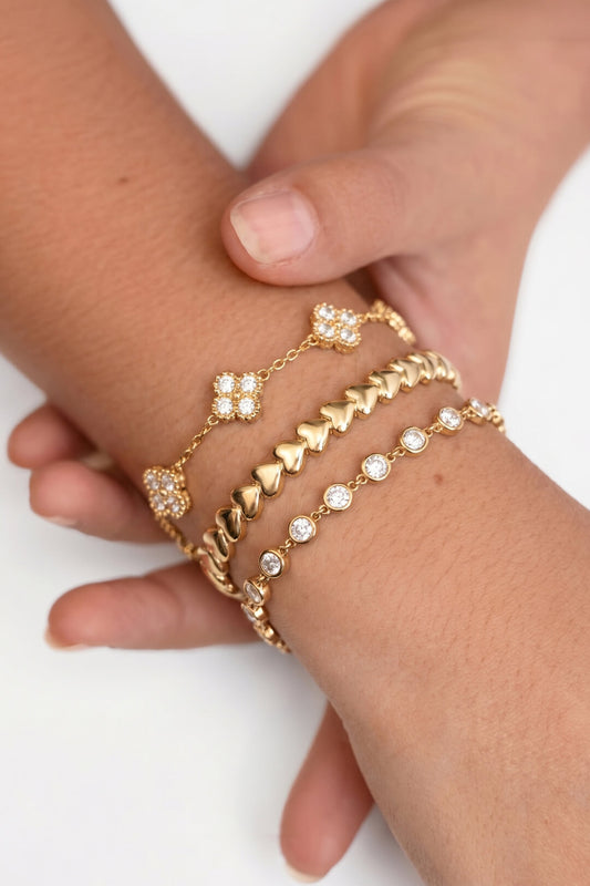 Stapelbare gouden armband met ronde zirkonia steentjes gedragen om pols met andere minimalistische armbandjes