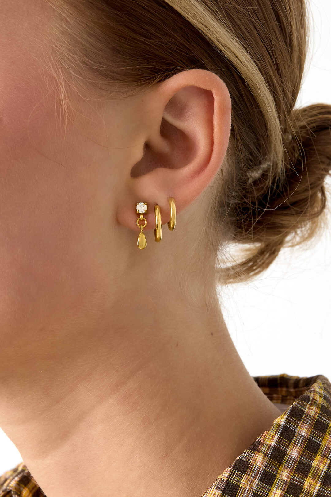 Vrouw draagt trendy stud oorbellen met druppel in de kleur goud. Gemaak van stainless steel.